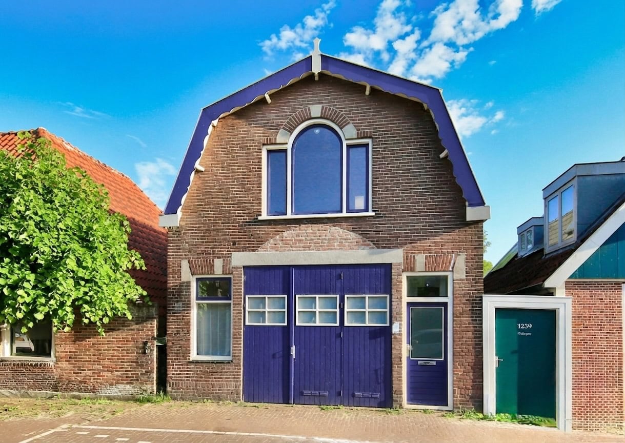 Een charmant huis met blauwe garage en grote ramen, gelegen aan de Sloterweg in Amsterdam.
